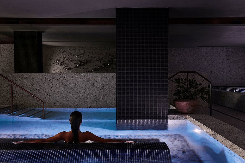 A person sitting inside a spa in a concrete heavy room.